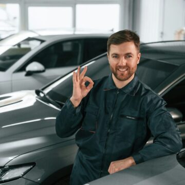 garagist-1 Un réparateur en uniforme se tient dans le garage avec des voitures.