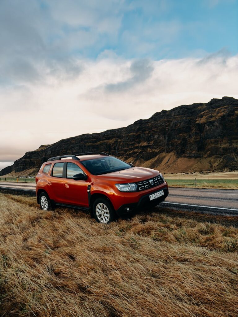 Un SUV orange vif garé dans un paysage islandais rural avec des collines dramatiques et une route ouverte.