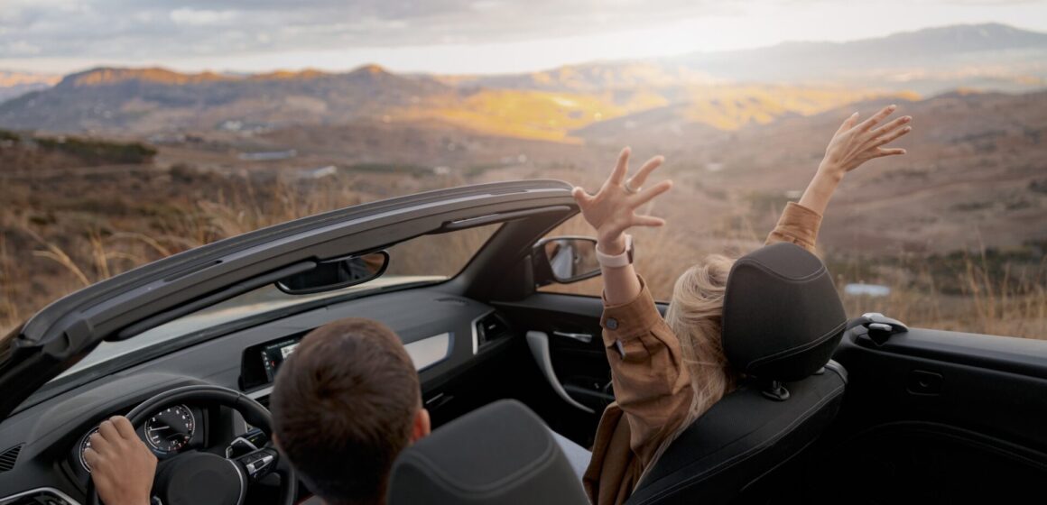 decapotable Arrière de couple homme et femme voyageant dans une voiture convertible à flanc de montagne profitant de la vue panorama