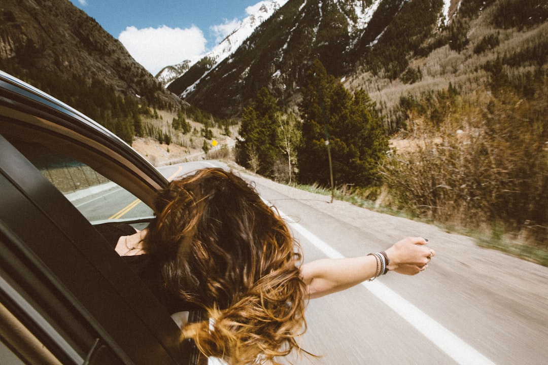 Femme conduisant sur un véhicule en mettant la tête et le bras droit à l'extérieur de la fenêtre en voyageant sur la route