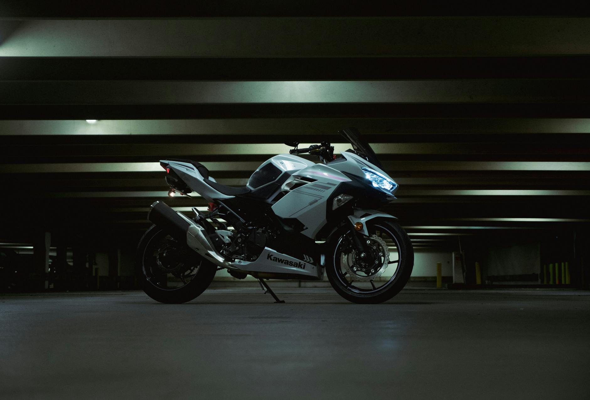 La moto Kawasaki blanche garée dans un parking sombre, présentant des design moderne et des lignes élégantes.