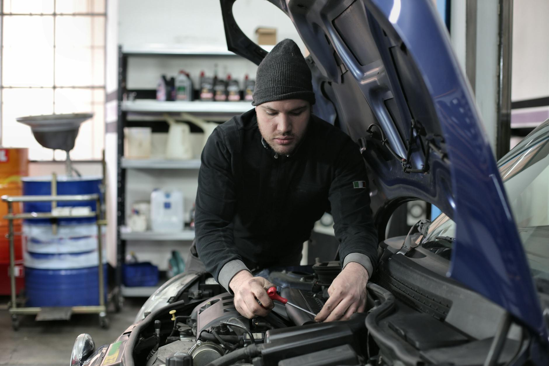 Homme travaillant sous le capot de voiture dans un garage, axé sur la réparation du moteur