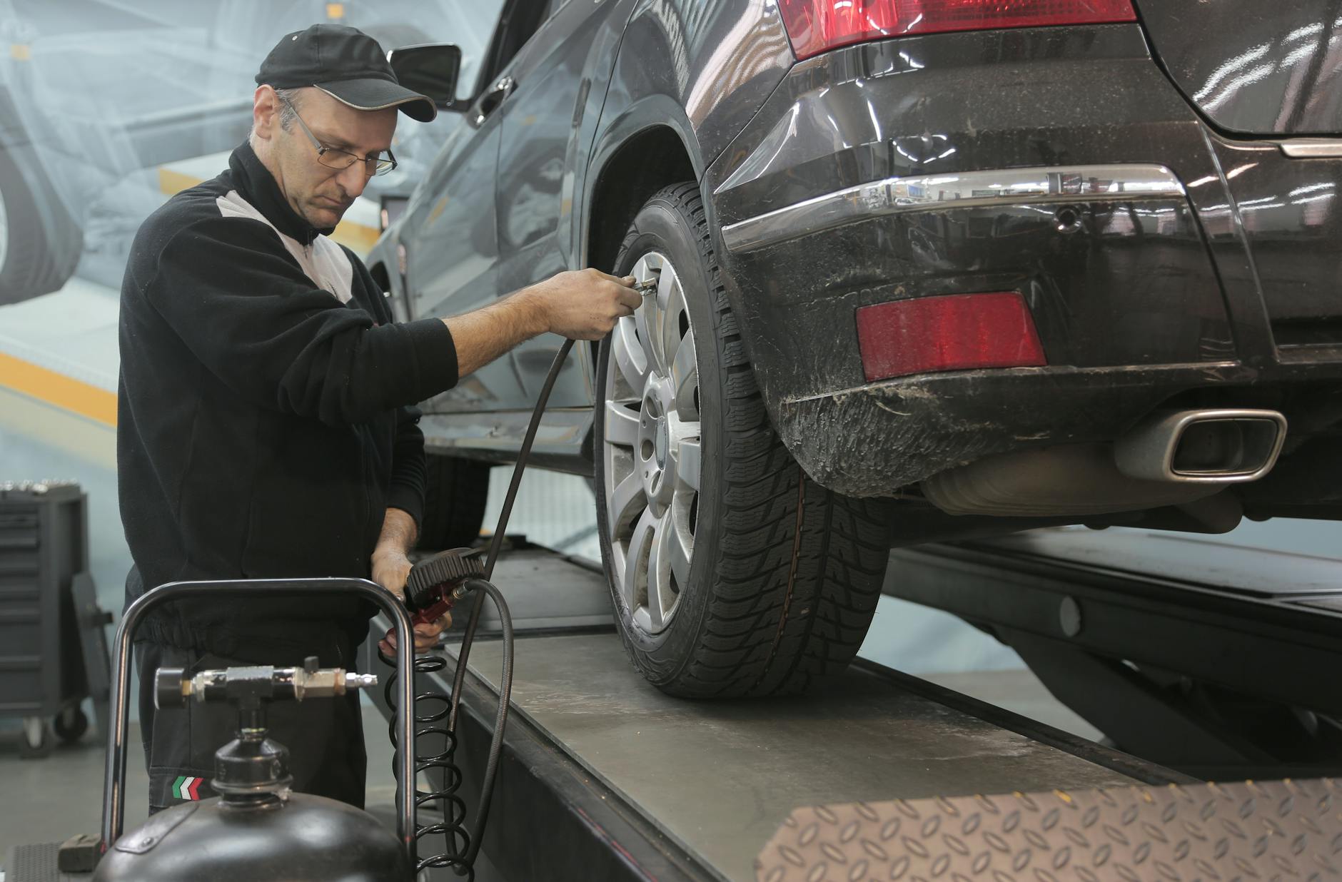 Un mécanicien masculin vérifie la pression des pneus sur un véhicule dans un atelier, présentant une expertise automobile.