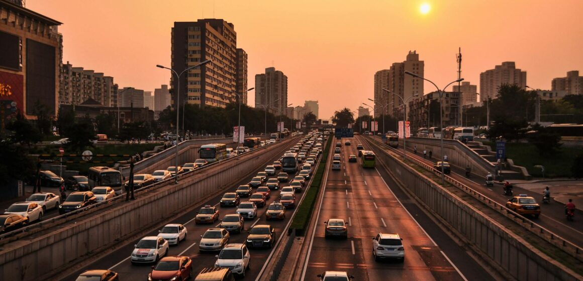 cars Une autoroute urbaine animée avec un trafic intense sous un ciel de coucher de soleil vibrant dans un fond de paysage urbain.