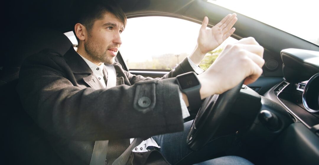 car-problem Homme conduisant une voiture, faisant un geste avec la main.