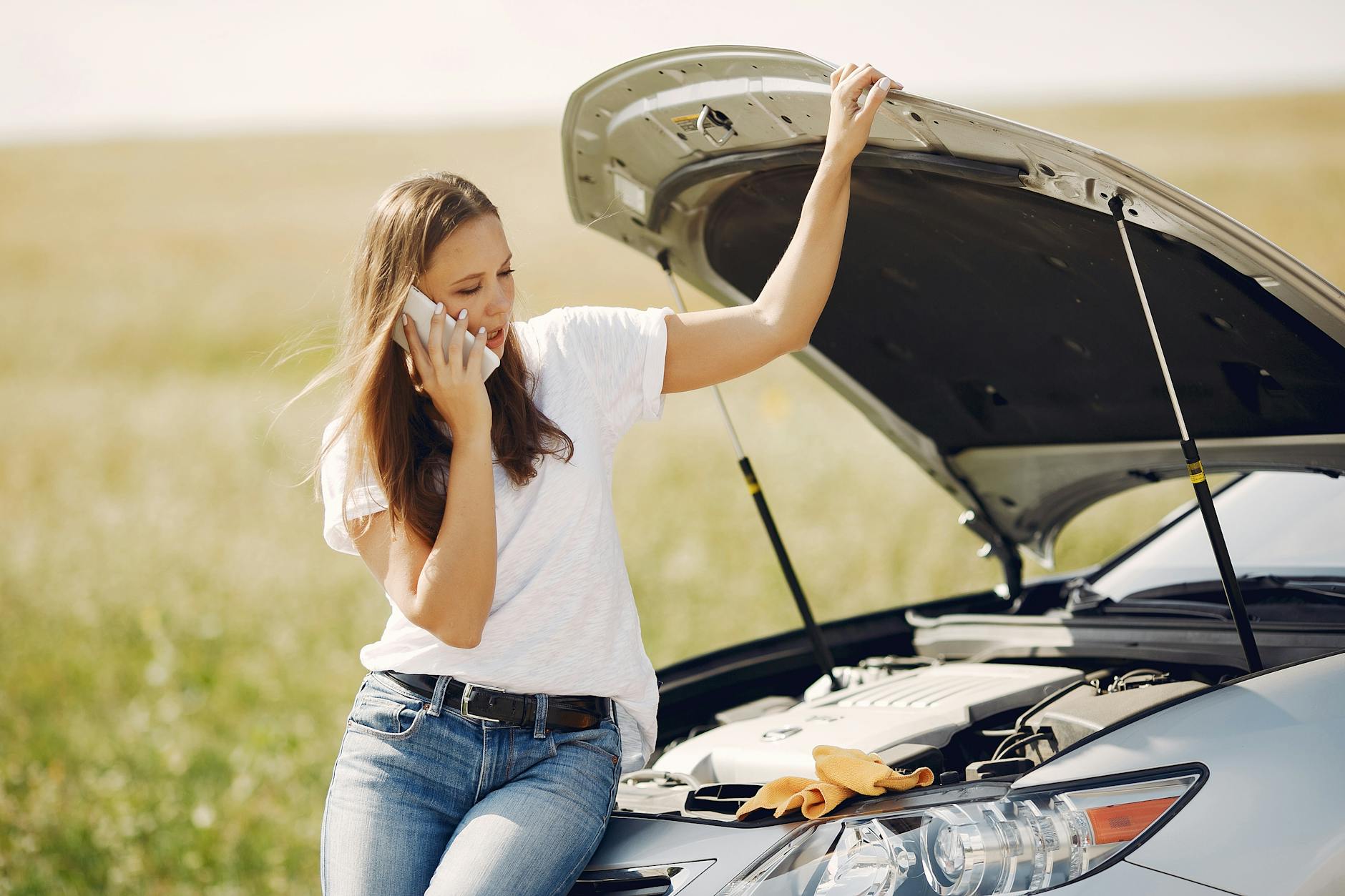 Jeune femme au téléphone demandant de l'aide pour la panne de voiture par une journée ensoleillée.