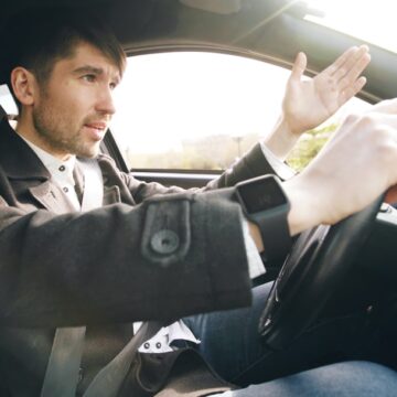car-problem Homme conduisant une voiture, faisant un geste avec la main.