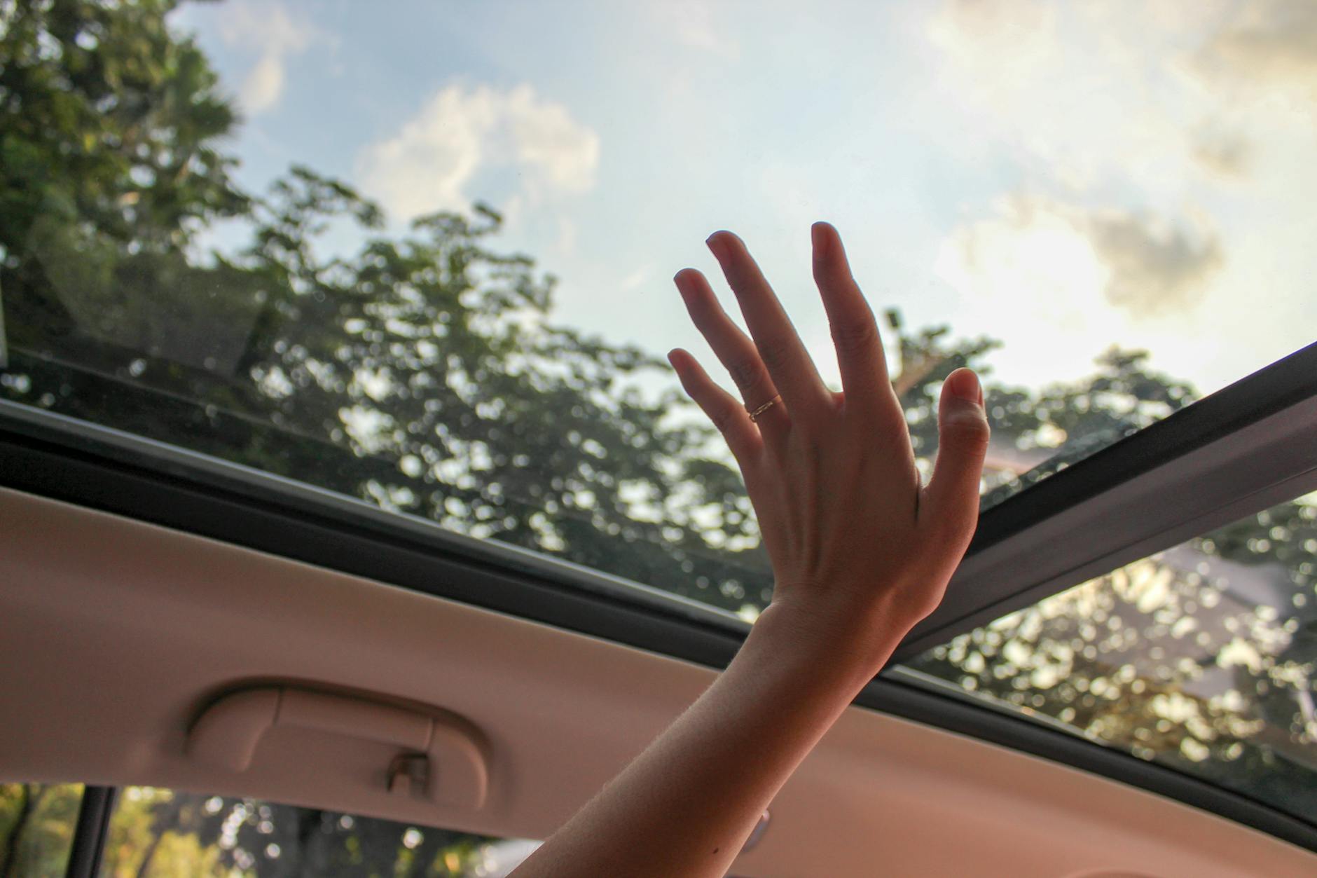 Une main tendant la main à travers un toit ouvrant de voiture, touchant le ciel par une journée ensoleillée.