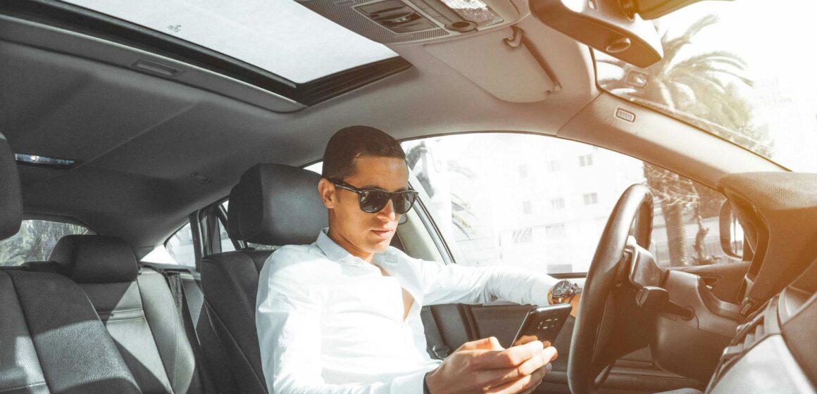 sunroof Un homme portant des lunettes de soleil sur son téléphone en conduisant une voiture au Maroc.