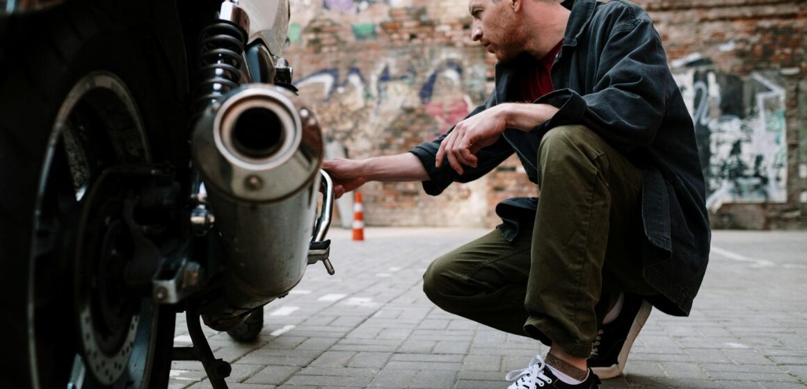 moto Un mécanicien accroupi pour examiner les gaz d'échappement d'une moto dans une zone urbaine extérieure.