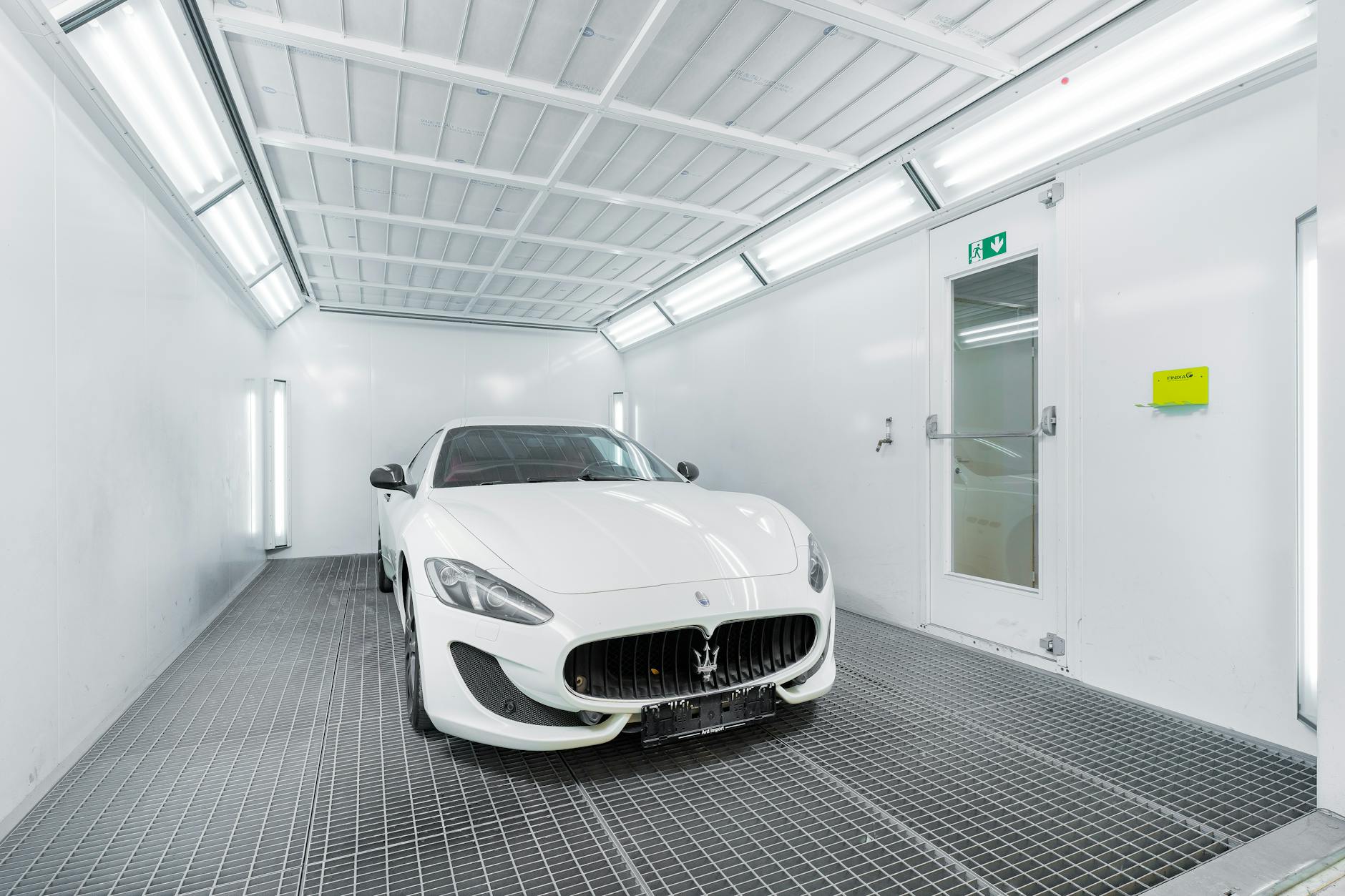 Voiture de luxe blanche dans une cabine de peinture bien éclairée, mettant en valeur un design élégant et sophistiqué.