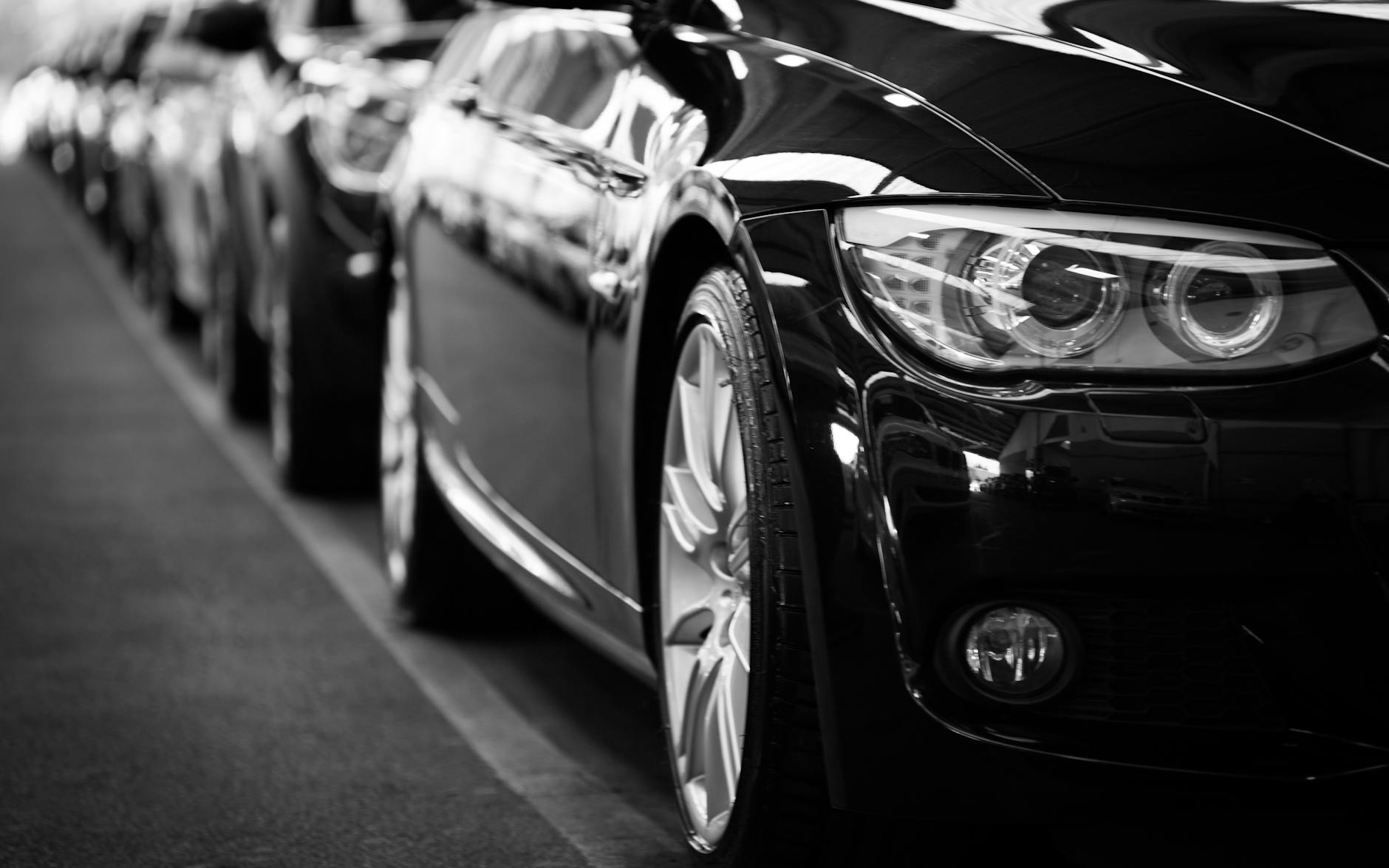 Image en gros plan en noir et blanc d'une gamme de voitures de luxe axée sur les phares des véhicules.