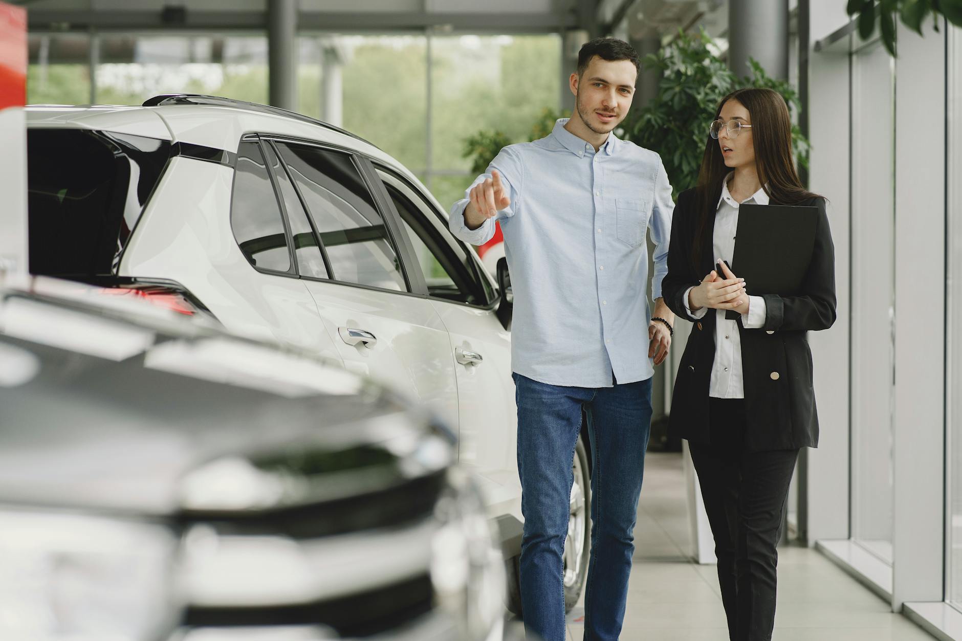 Client et vendeur discutant d'un véhicule dans la salle d'exposition d'un concessionnaire automobile moderne.