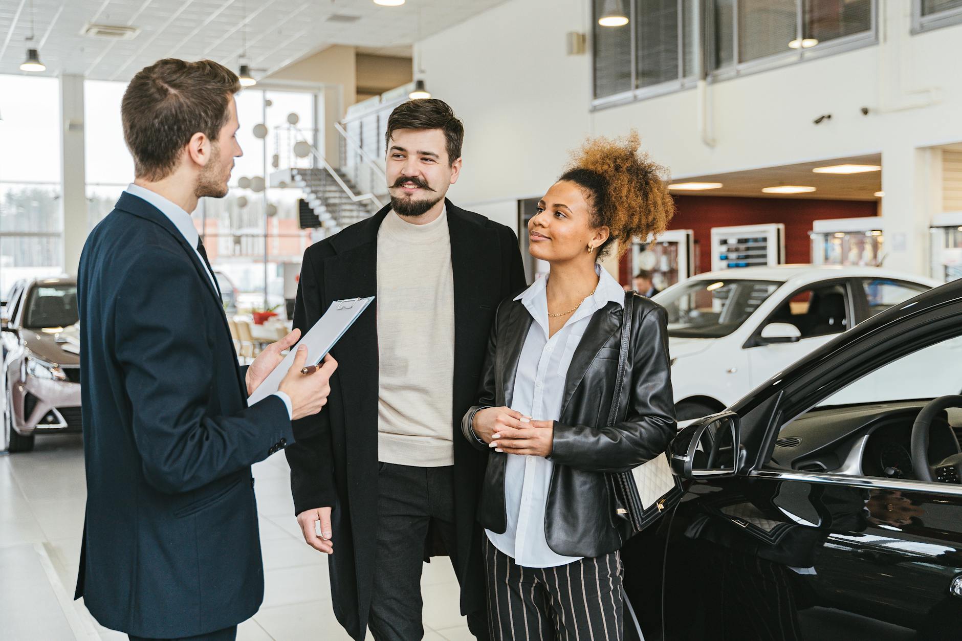 Couple discutant de l'achat d'une voiture avec un vendeur chez un concessionnaire intérieur, engageant une conversation.