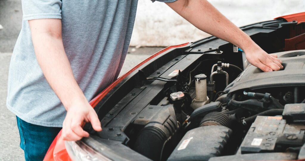 Un homme inspecte le moteur d’une voiture, probablement en cas de panne d’urgence.