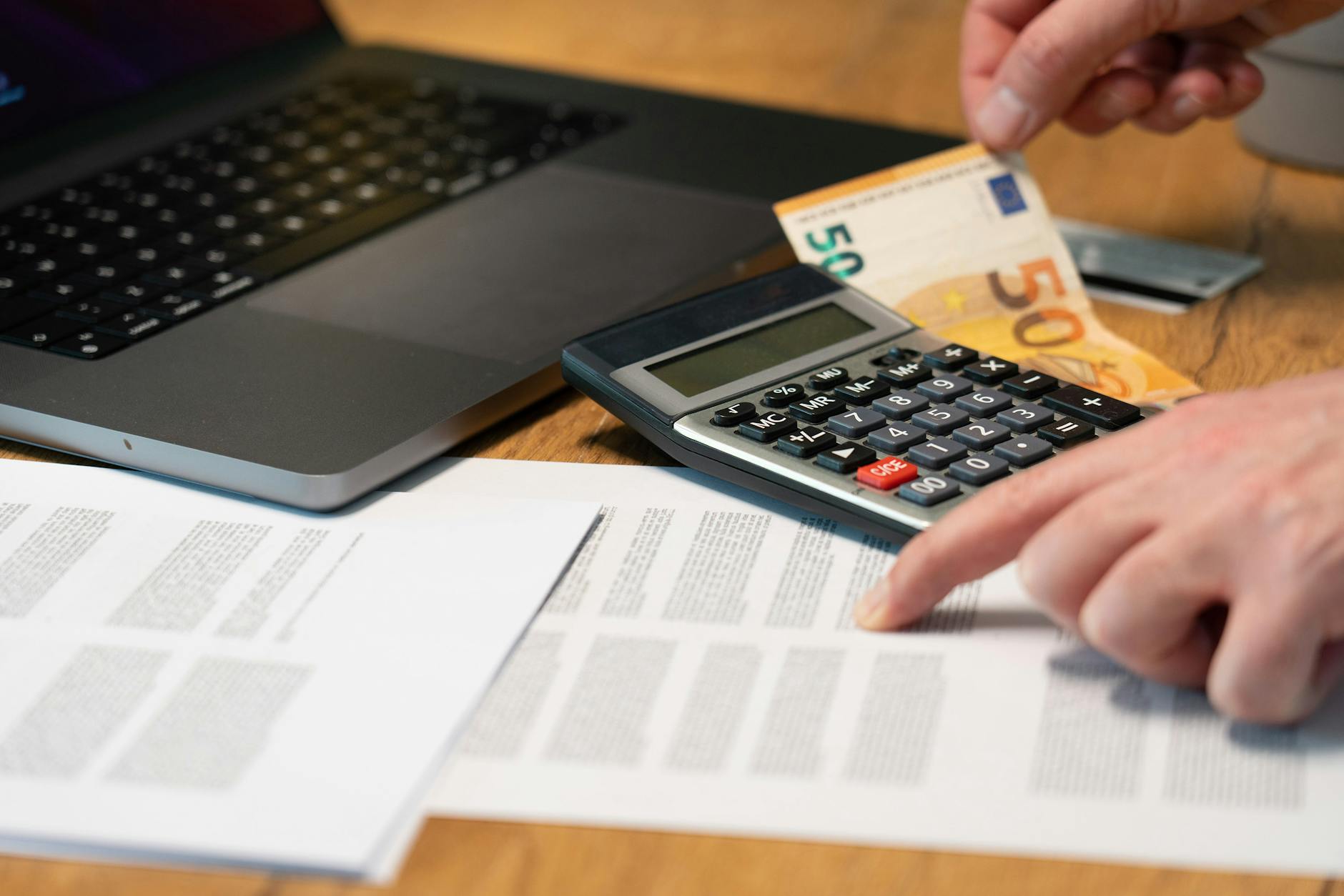 Gros plan des mains à l'aide d'une calculatrice avec des billets en euros et un ordinateur portable sur le bureau.
