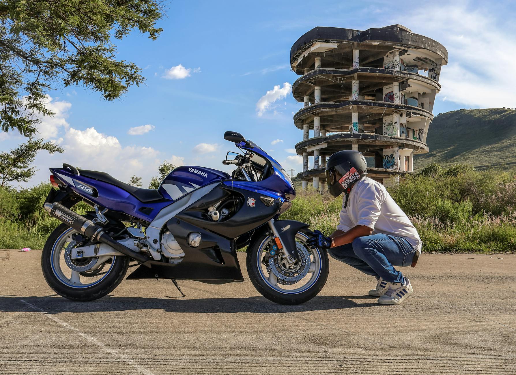 L'homme ajuste la moto près d'un bâtiment abandonné par beau temps.