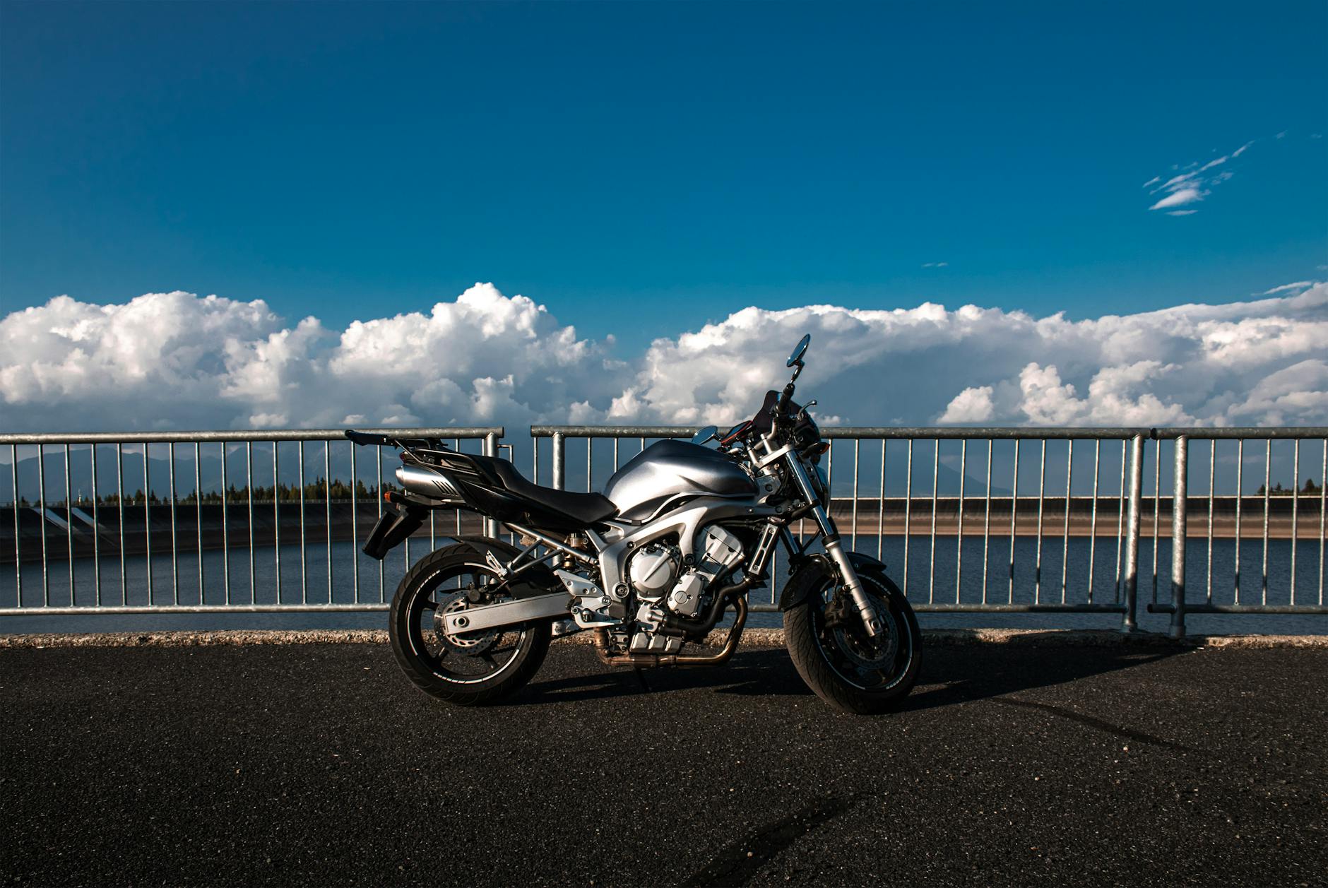 Moto argentée élégante garée sur une route côtière avec un décor pittoresque d'eau et de nuages, incarnant la liberté par temps clair.