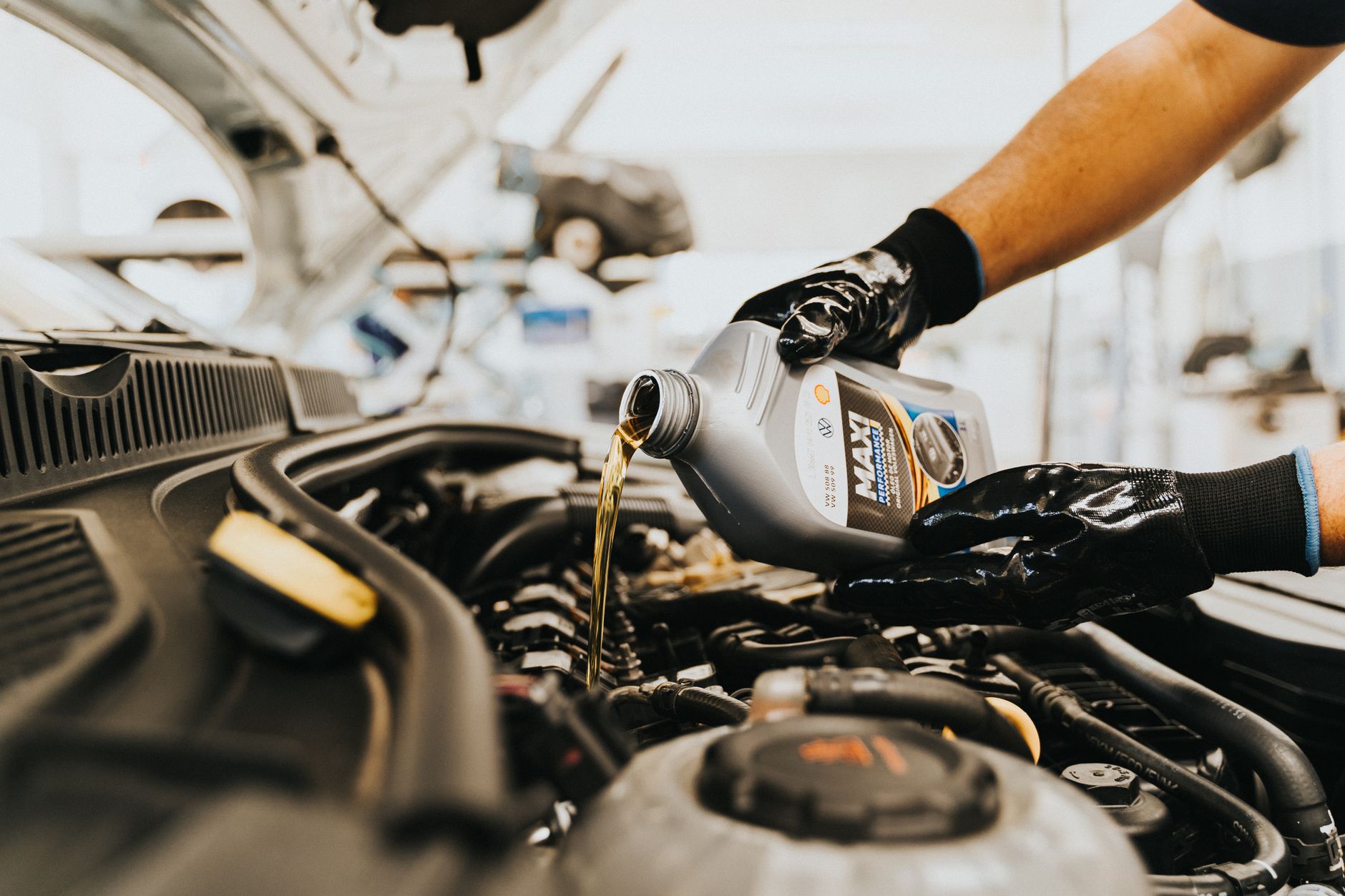 Gros plan d'un mécanicien versant de l'huile moteur dans un moteur de voiture dans un atelier de réparation automobile.