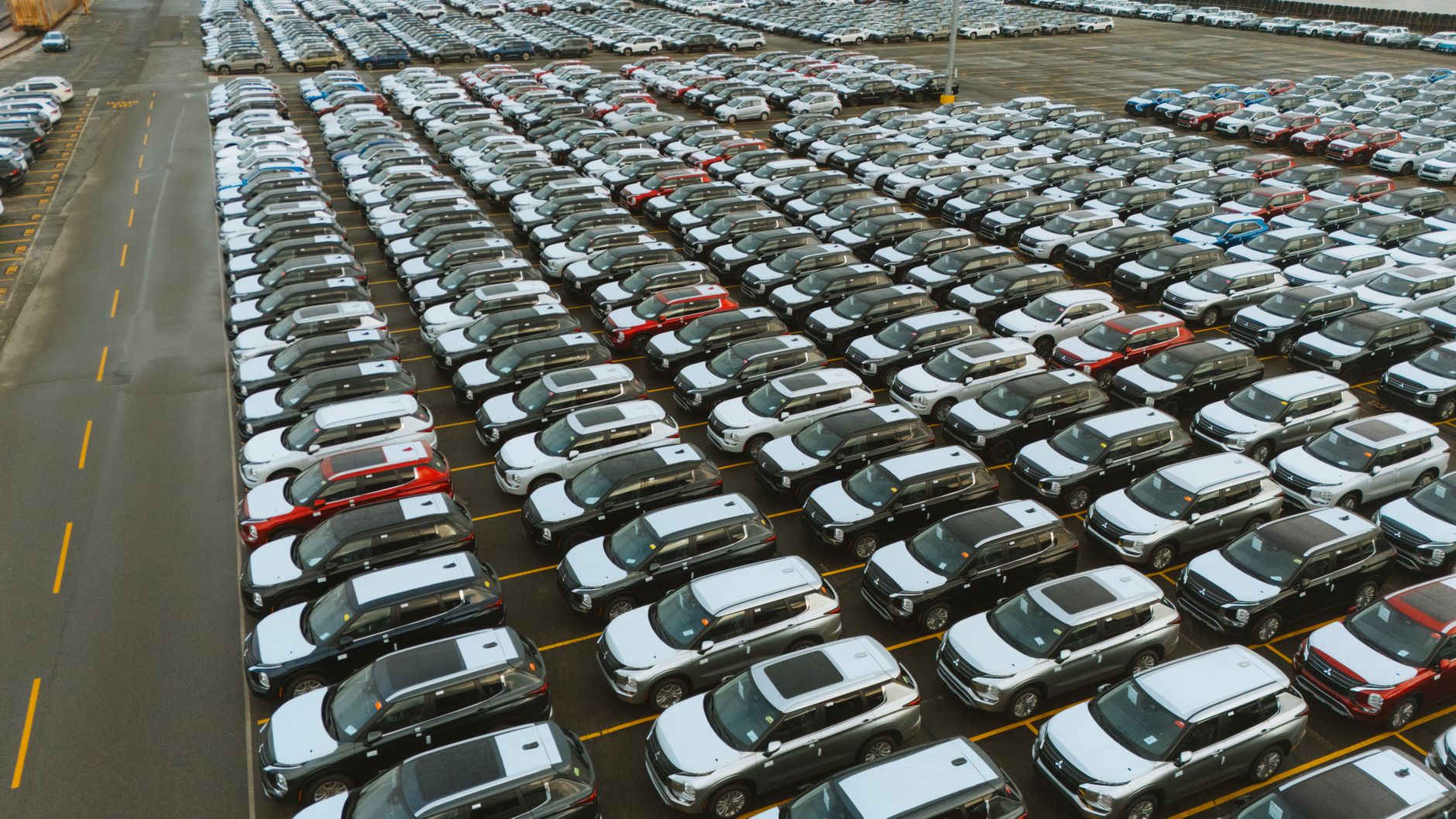 Prise de vue aérienne d'un vaste parking rempli de véhicules neufs prêts à être distribués.
