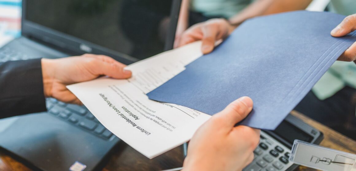 Changement-de-titulaire Gros plan sur des mains échangeant des documents immobiliers dans un bureau.