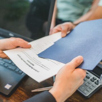 Changement-de-titulaire Gros plan sur des mains échangeant des documents immobiliers dans un bureau.