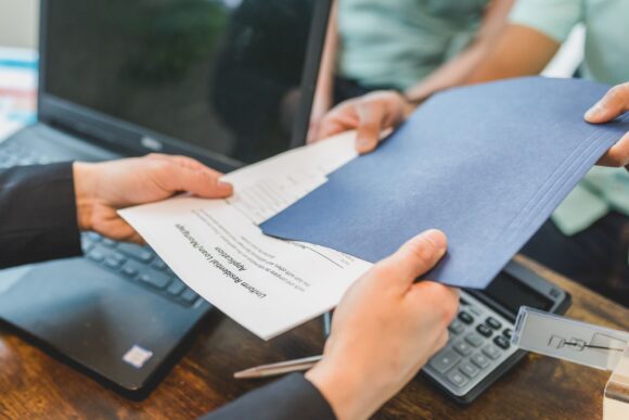 Changement-de-titulaire Gros plan sur des mains échangeant des documents immobiliers dans un bureau.
