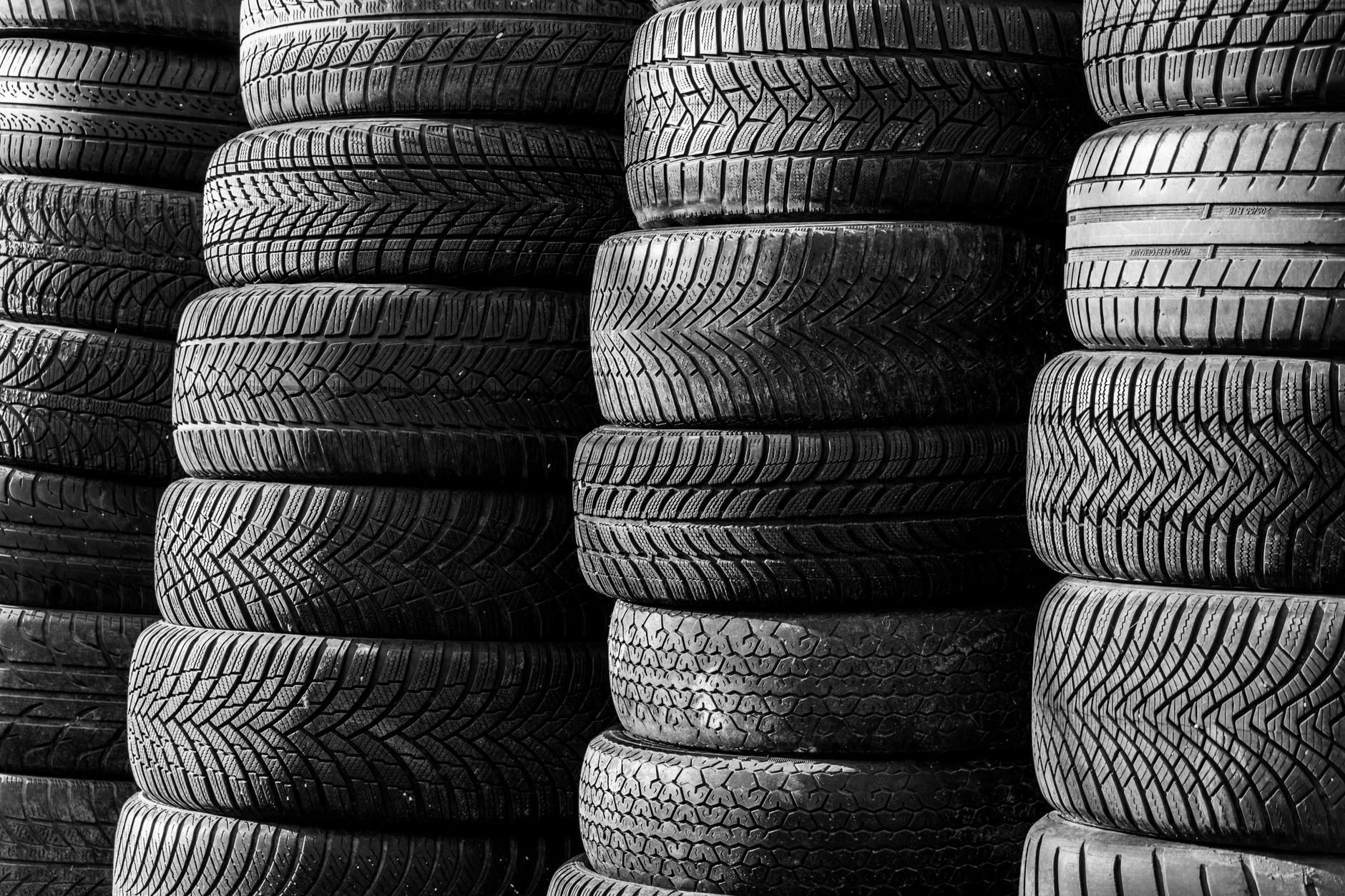 Image en noir et blanc de pneus de véhicule empilés présentant différents motifs de bande de roulement.