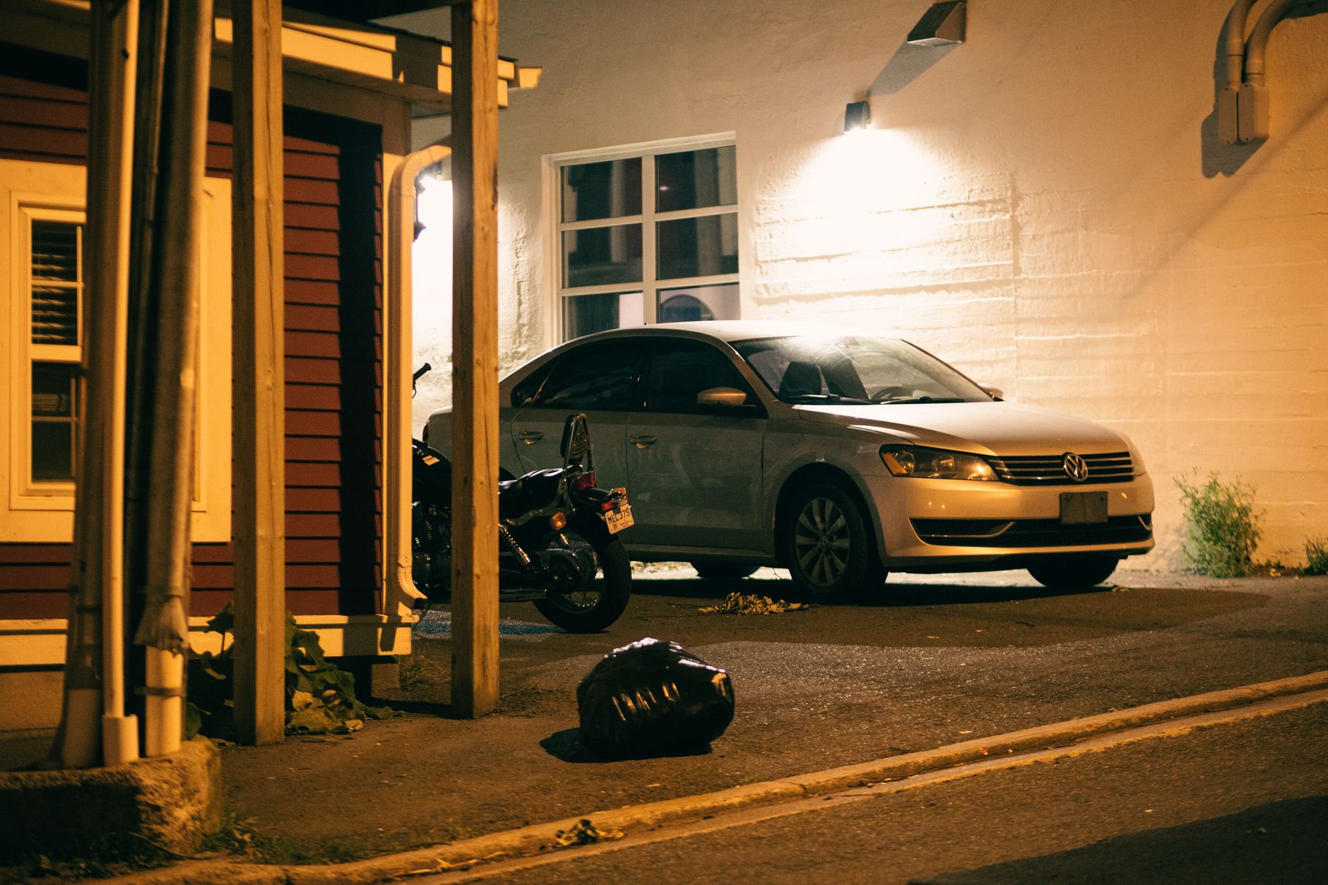 Voiture et moto Volkswagen garées dans une zone urbaine faiblement éclairée la nuit.